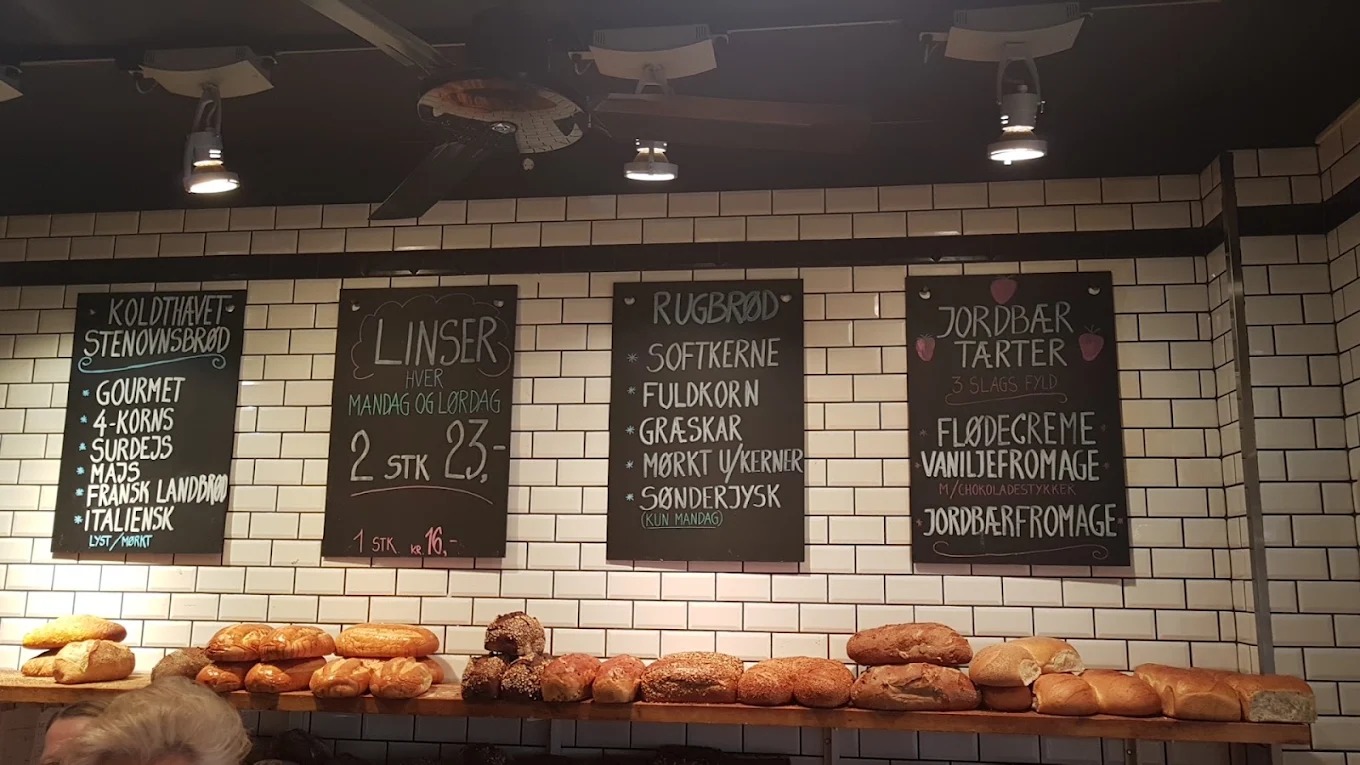 Tavler med brødsorter over hylder med friskbagt brød i Wiuff Bageri